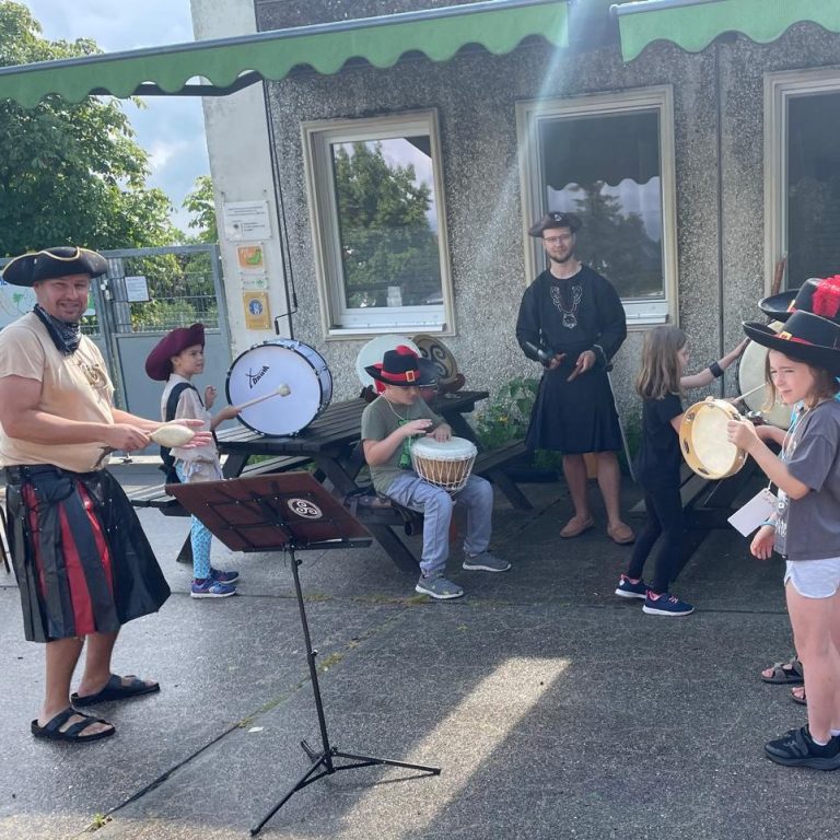 Musiker in historischen Kostümen spielen verschiedene Instrumente im Freien.