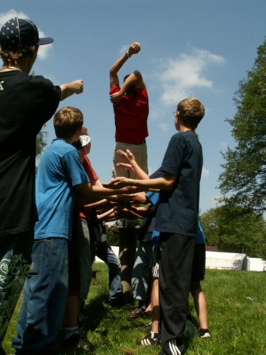 Kinder stehen in einer Gruppe und helfen einem Jungen, der in der Luft schwebt.