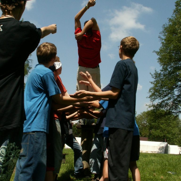 Gruppe von Kindern hebt einen Jungen in rotem Shirt zum Üben von Teamarbeit.