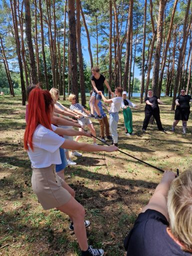 Gruppenspiel im Wald, Teilnehmer ziehen an einem Seil unter einem sonnigen Himmel.