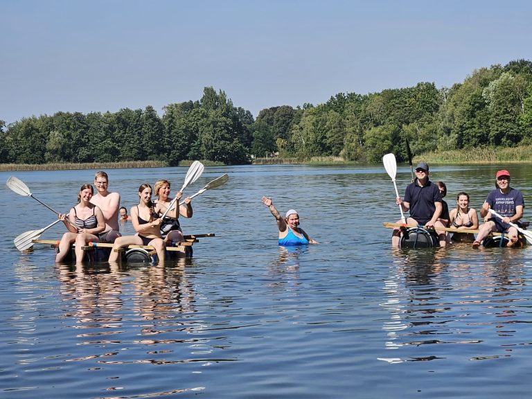 Gruppe von Menschen rudert auf einem ruhigen Gewässer bei sonnigem Wetter.