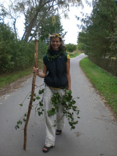 Eine Person mit einem Stock und Zweigen in der Hand, die auf einem Weg steht.