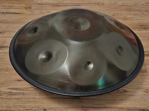 Handpan mit mehreren konkaven Oberflächen, auf einem Holzuntergrund platziert.