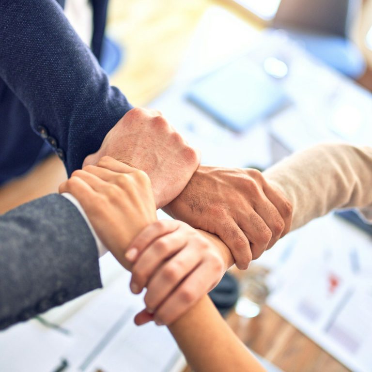 Verschränkte Hände mehrerer Personen im Büro, Symbol für Teamarbeit und Zusammenarbeit.