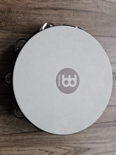 Runde Tambourine mit einem zentralen Logo auf der Oberseite, auf einem Holzboden.