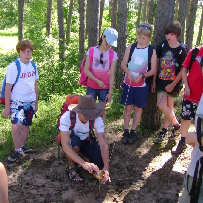 Gruppe von Kindern und einem Erwachsenen beim Forschen im Wald.