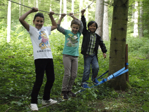 Drei Kinder spielen im Wald und halten sich an einer Schnur fest.