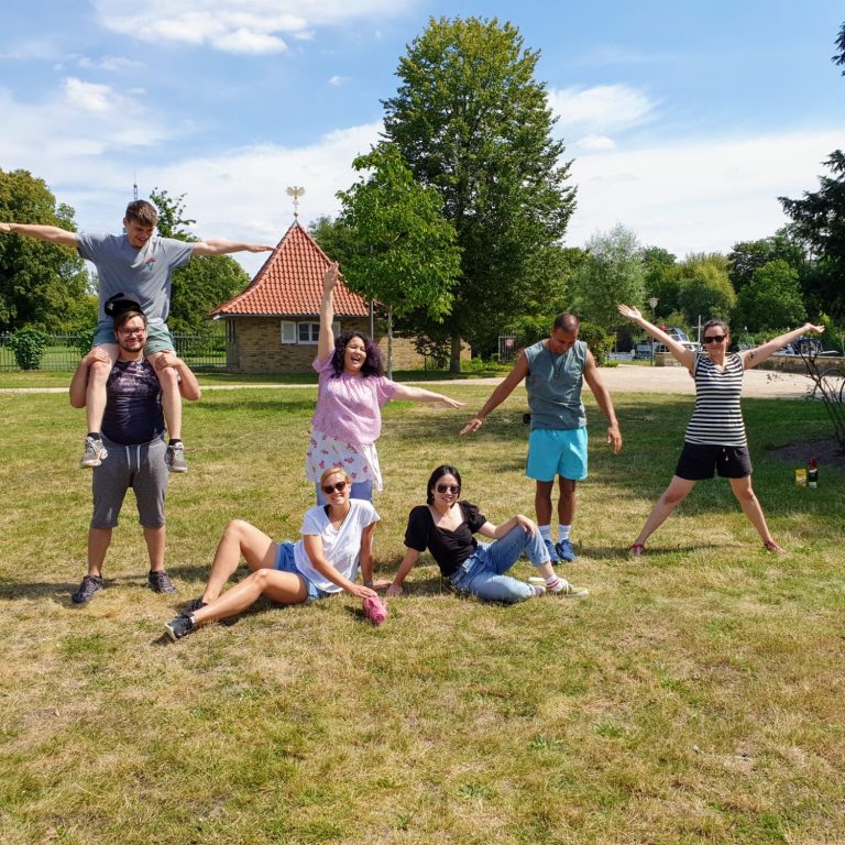 Gruppe von Menschen in einem Park, einige stehen, andere liegen, alle lächeln.