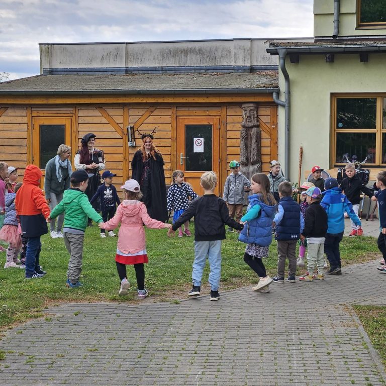 Kinder stehen im Kreis, während Erwachsene in Kostümen eine Aufführung präsentieren.