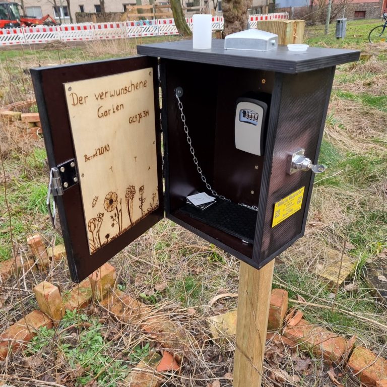 Offenes, schwarzes Gartenhäuschen mit Zähler und Kabel auf einem Holzpfahl.