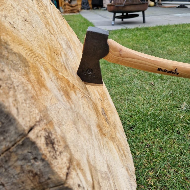 Eine Axt steckt in einem großen Holzblock auf einer grünen Wiese.