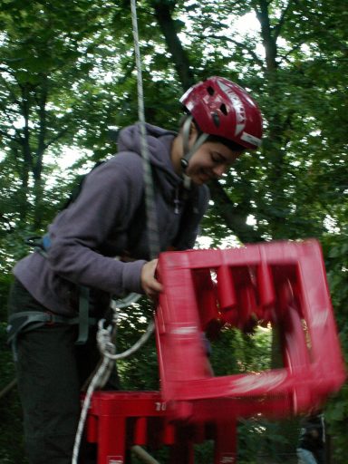 Person mit Helm befestigt eine rote Struktur in einer Waldumgebung.