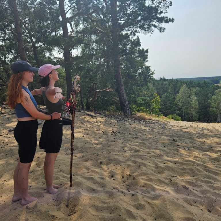 Zwei Personen stehen auf einem Sandhügel und blicken in die Ferne.